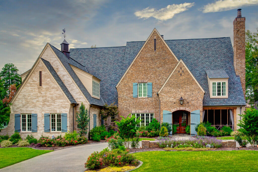 French Tudor home in Chenal, Little Rock AR. Home has soft, warm light blues and greens. The gabled faces are warm yellow brick and stone. 